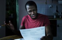 High taxes concept. Young frustrated african american man looking at utility bill, worried about troubles with mortgage payment to bank, having serious problems with debt